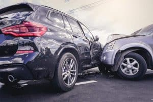 Two cars involved in a collision; the front of a silver vehicle has impacted the side of a black SUV in a parking lot.
