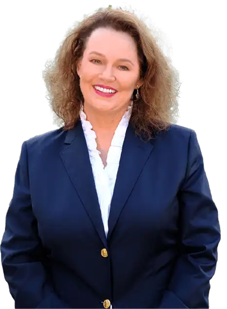 A woman with curly brown hair, wearing a navy blazer and white ruffled blouse, smiles while standing and facing the camera.