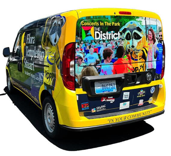 A yellow van displays advertisements for Flora Templeton Stuart Accident Injury Lawyers, featuring a mascot, concert promotion, legal service details, and highlighting their Giving Back To The Community program.