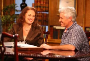 A woman and a man sit at a wooden table in Kentucky, smiling and talking about a personal injury case, with bookshelves and papers visible in the background.