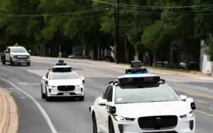 Three self-driving cars equipped with sensors and cameras drive down a city street surrounded by trees, illustrating Kentucky’s embrace of autonomous technology and raising important questions about liability.