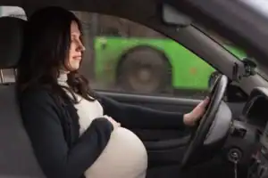 Pregnant woman sitting in the driver’s seat of a car in Bowling Green, holding the steering wheel with one hand and her belly with the other—highlighting concerns about car accidents during pregnancy.