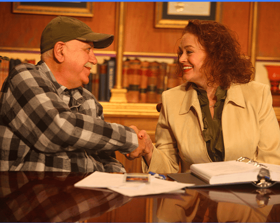 Two people sit at a table in Elizabethtown KY, smiling and shaking hands, with paperwork and books visible in the background—perhaps discussing their case with experienced truck accident lawyers.