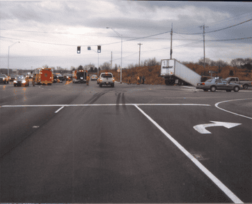 A truck is off the road on a slight embankment near an intersection in Bowling Green, KY, with emergency vehicles and cars stopped nearby under a cloudy sky.