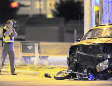 A police officer photographs the scene of a nighttime accident involving a damaged car and motorcycle on a city street, evidence that may be used by Motorcycle Accident Lawyers in Bowling Green KY.