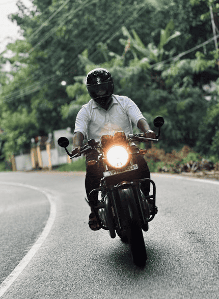 A person wearing a helmet and white shirt rides a motorcycle on a curved road surrounded by greenery, much like the scenic routes near Bowling Green KY—where Motorcycle Accident Lawyers are ready to help when needed.
