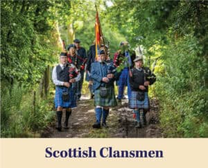 A group of men in traditional Scottish attire, including kilts, march down a wooded path playing bagpipes and drums, reminiscent of a heritage parade Judge Clay Elliott or Flora Templeton Stuart might attend.