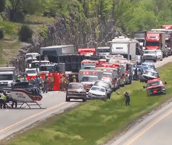 Emergency vehicles, including ambulances, fire trucks, and police cars, respond to a major truck accident on a Bowling Green highway; a medical helicopter is also present, with traffic backed up behind the scene.