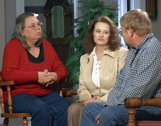Three adults sit indoors in Bowling Green, KY, engaged in conversation. One woman wears a red sweater, another a beige jacket, and a man in glasses and a plaid shirt. Plants and furniture are visible—perhaps discussing motorcycle accident lawyers.