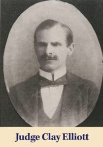 Black and white portrait of a stern-faced man in formal attire with a bow tie, labeled "Judge Clay Elliott." Known for tracing his roots from Scotland to Louisiana, he stands as a symbol of integrity and legacy.