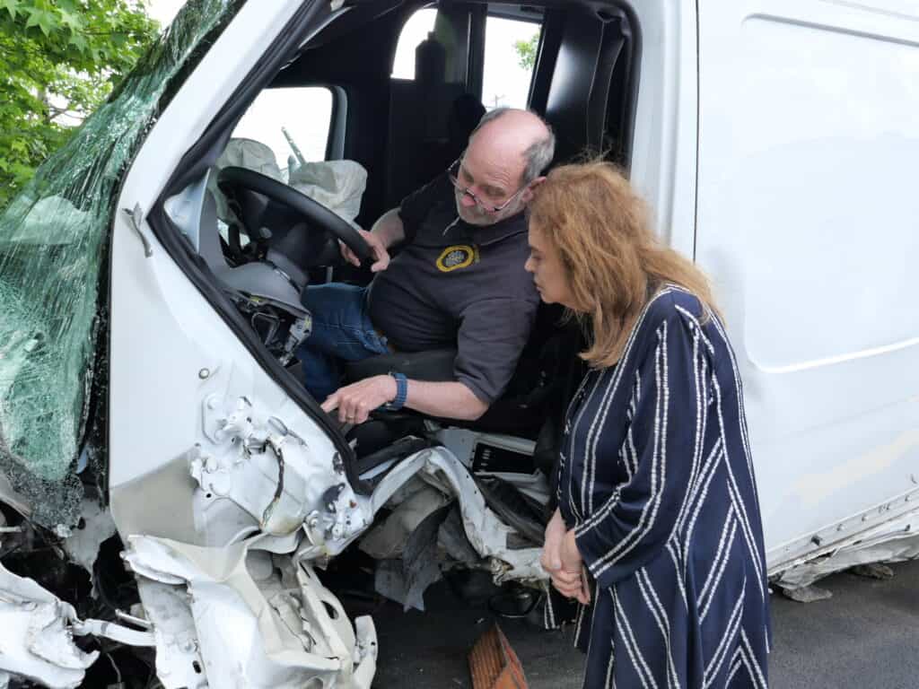 A man sitting in a damaged vehicle shows something on the dashboard to a woman standing outside, both examining the crash site—typical of cases handled by KY Truck Accident Lawyers in Bowling Green.