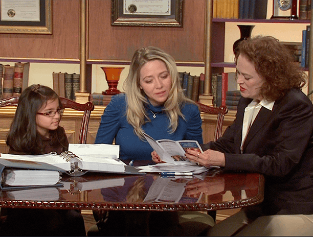 Three people sit at a table with open binders and documents, having a discussion in a Bowling Green, KY office lined with bookshelves and framed certificates—an environment reflecting dedicated car accident lawyers at work.