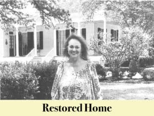 Woman standing in front of a large, restored Louisiana house with columns and a porch, surrounded by landscaped bushes and trees. Text at the bottom reads "Restored Home." Virginia Settlers history is reflected in the elegant architecture.
