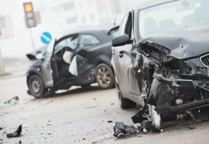 Two heavily damaged cars are shown after a collision at an intersection, with debris scattered on the road and airbags deployed.